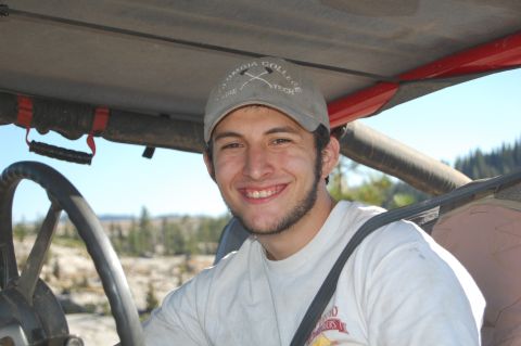 1993 Jeep Wrangler - A smiling man sits in the driver's seat of a vehicle, wearing a baseball cap and a t-shirt.