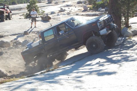 1993 Jeep Wrangler - This lifted pickup truck navigates a rocky incline, kicking up dust. Another off-road vehicle is visible in the background.