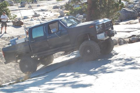 1993 Jeep Wrangler - Modified pickup truck navigates a challenging off-road course with large boulders and trees.