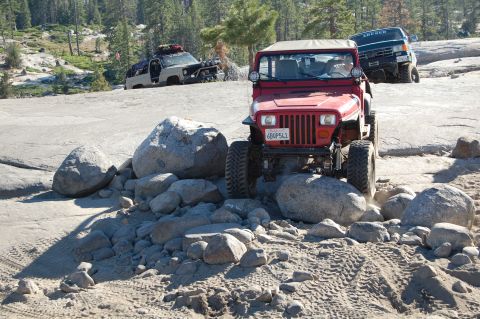 1993 Jeep Wrangler - Multiple off-road vehicles tackle a rocky terrain, with a red Jeep Wrangler in the foreground.