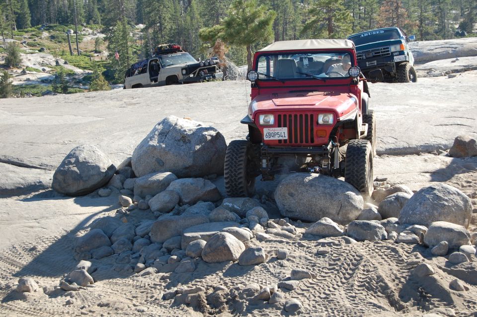 Red 1993 Jeep Wrangler navigating rocks on a trail, with another Jeep and a van behind it