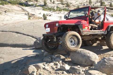 1993 Jeep Wrangler - A red 1993 Jeep Wrangler navigates a rocky trail, demonstrating its off-road capability.