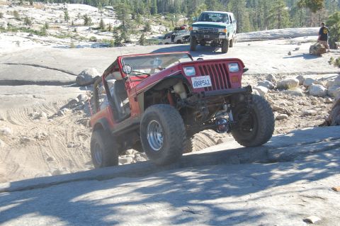 1993 Jeep Wrangler - This red Jeep Wrangler is navigating a rocky off-road trail with other vehicles present.