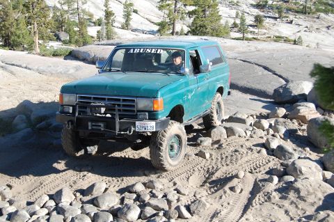 1993 Jeep Wrangler - A green Ford Bronco navigates a rocky trail, its "ABUSED" windshield sticker visible.