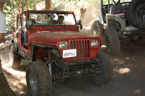 1993 Jeep Wrangler - This red 1993 Jeep Wrangler navigates a dusty off-road path, with another vehicle visible behind it.