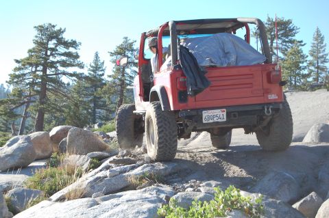 1993 Jeep Wrangler - A red Jeep Wrangler navigates a rocky off-road trail under a clear blue sky.