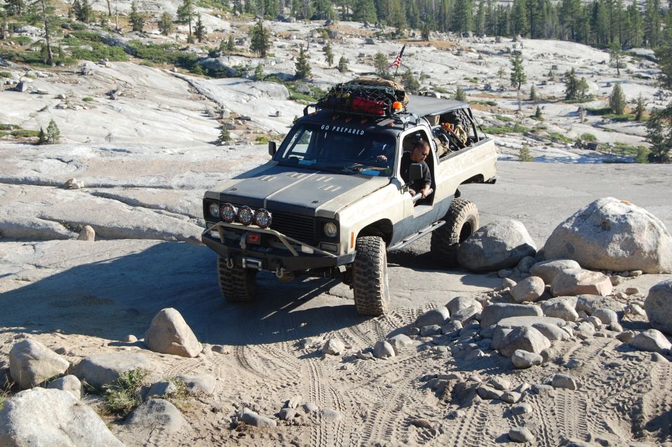 Modified pickup truck with roof rack and off-road tires navigating rocky terrain