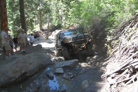 1993 Jeep Wrangler - A group of people watch as an off-road vehicle tackles a challenging, rocky path in a forest.