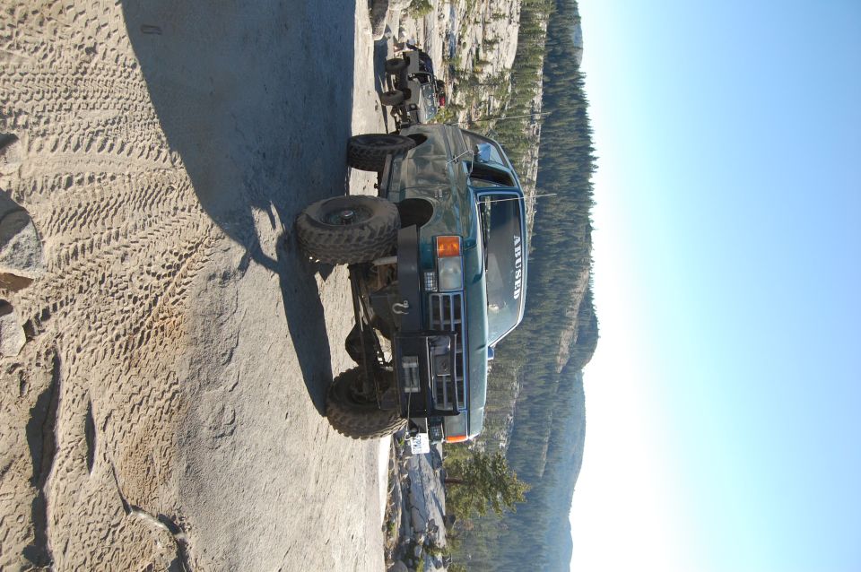 Green off-road SUV with large tires on a rocky mountain trail. Text on windshield reads 'AHUNED'