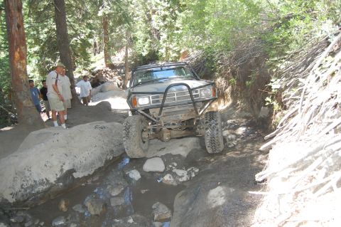 1993 Jeep Wrangler - Off-road truck navigating a challenging rocky path in a forest setting.