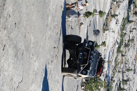 1993 Jeep Wrangler - A modified Jeep Wrangler is positioned precariously on a sheer rock face, with a person observing from above.