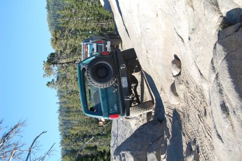 1993 Jeep Wrangler - Ford Bronco navigating a challenging rocky incline on a sunny day.