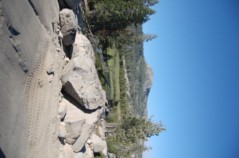 1993 Jeep Wrangler - Tire tracks mark a path through a rocky landscape, with trees and mountains under a clear blue sky.