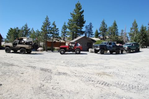 1993 Jeep Wrangler - A collection of off-road vehicles, including a red Jeep, a tan SUV, and two trucks, are parked in a dusty lot on a clear day.