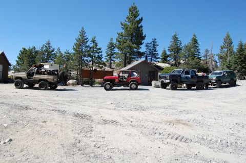 1993 Jeep Wrangler - Multiple off-road vehicles are parked in a dirt lot on a sunny day.