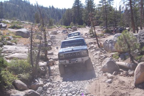 1993 Jeep Wrangler - Multiple off-road vehicles navigate a challenging rocky path in a wooded area.