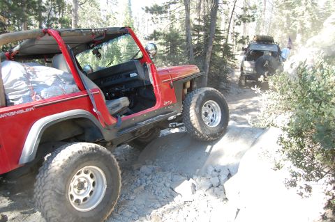 1993 Jeep Wrangler - Two red Jeep Wranglers navigate a challenging rocky trail in a wooded area.