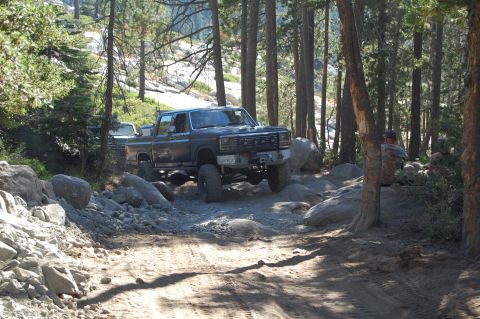 1993 Jeep Wrangler - Pickup truck navigates a challenging rocky path in a wooded area, with another vehicle visible.