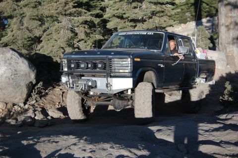 1993 Jeep Wrangler - Modified Ford F-Series truck navigating rough terrain with a driver visible.