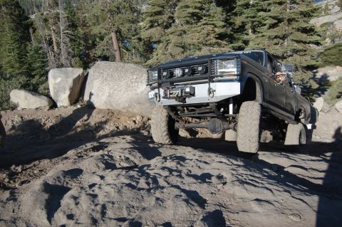 1993 Jeep Wrangler - A heavily modified pickup truck navigates a challenging rocky terrain on a sunny day.