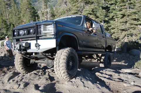 1993 Jeep Wrangler - A modified black pickup truck navigates a challenging rocky terrain with a driver visible inside.
