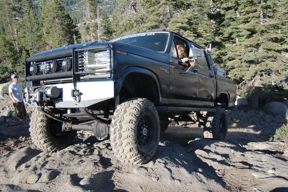 Black lifted pickup truck with custom bumper and winch, driving on a rocky trail