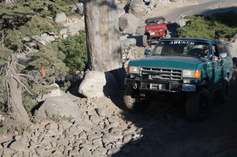 1993 Jeep Wrangler - A green SUV navigates a challenging rocky terrain, with a red Jeep following closely behind on the trail.