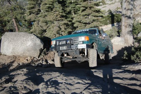 1993 Jeep Wrangler - Modified Ford F-150 navigates a challenging rocky path. The grille suggests a 1992 model year.