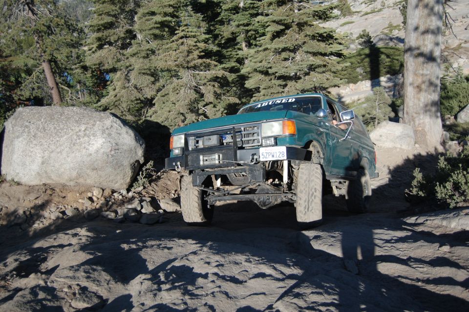 Green Ford F-150 off-roading on a rocky trail, front bumper modified with a winch. License plate reads 52PW128