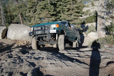 1993 Jeep Wrangler - This Ford Bronco is navigating a challenging, rocky off-road terrain with large boulders and trees surrounding it.