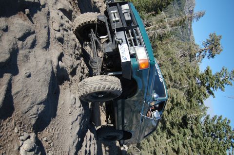 1993 Jeep Wrangler - This off-road vehicle navigates a steep, rocky incline with trees and mountains in the background.