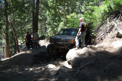 1993 Jeep Wrangler - An off-road SUV is shown on a challenging rocky trail in a wooded area.