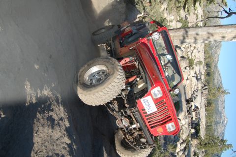 1993 Jeep Wrangler - Red 1993 Jeep Wrangler navigating a challenging off-road course with rocky terrain and trees.