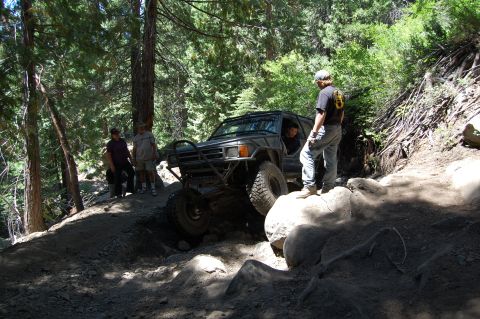 1993 Jeep Wrangler - A modified off-road vehicle tackles a challenging rocky trail in a wooded area.
