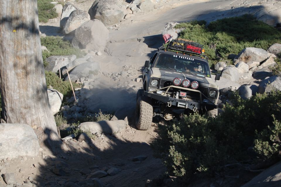 Gray Jeep CJ-7 off-roading on a rocky trail, with a winch and extra lights