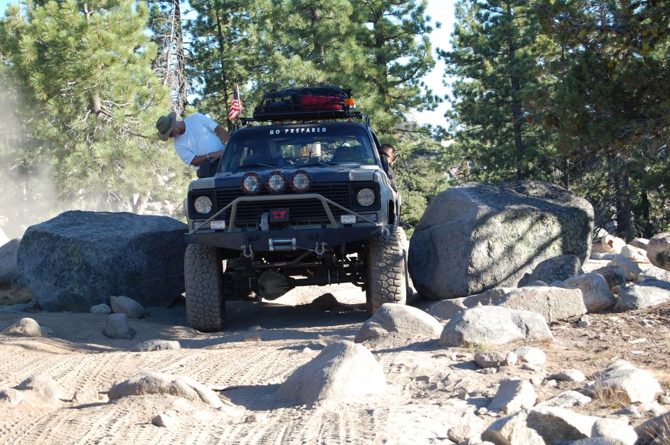 Black off-road vehicle with winch and roof rack navigating rocky terrain