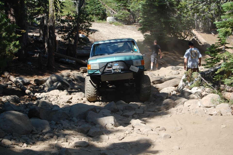 Ford Bronco off-roading on a rocky trail with two people watching