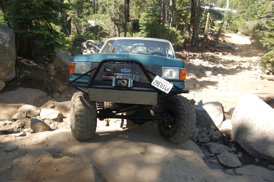 Teal off-road vehicle with a winch and aftermarket bumper on a rocky trail