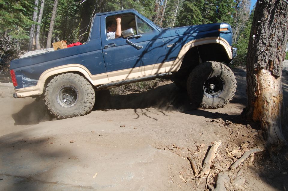 Blue Ford Bronco with tan stripe climbing over dirt and rocks, driver visible