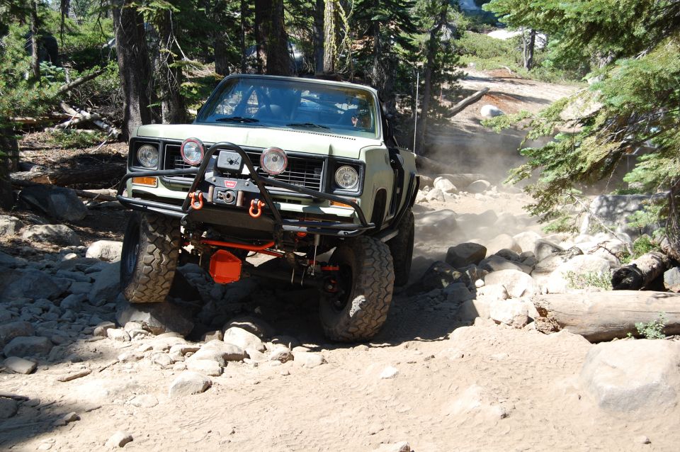 Off-road truck with winch and lights navigating a rocky trail, kicking up dust