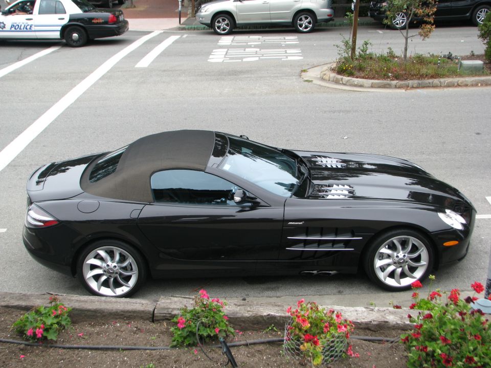 Black convertible sports car with a black soft top, side vents, and multi-spoke wheels parked curbside