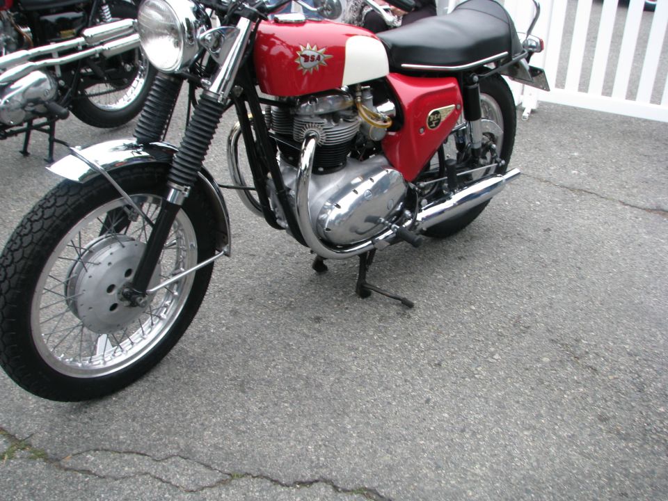 Red and white BSA motorcycle parked on asphalt. Another motorcycle is visible behind it