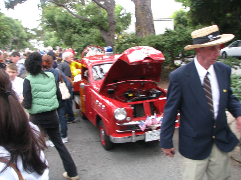 Red vintage fire truck with hood open, parked on a street with people around. American flags adorn the front