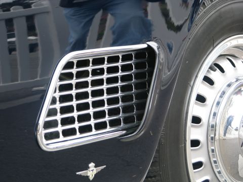 2004 Chrysler PT Cruiser - Detail shot of a car's fender vent and wheel, with a reflection of a person in jeans.