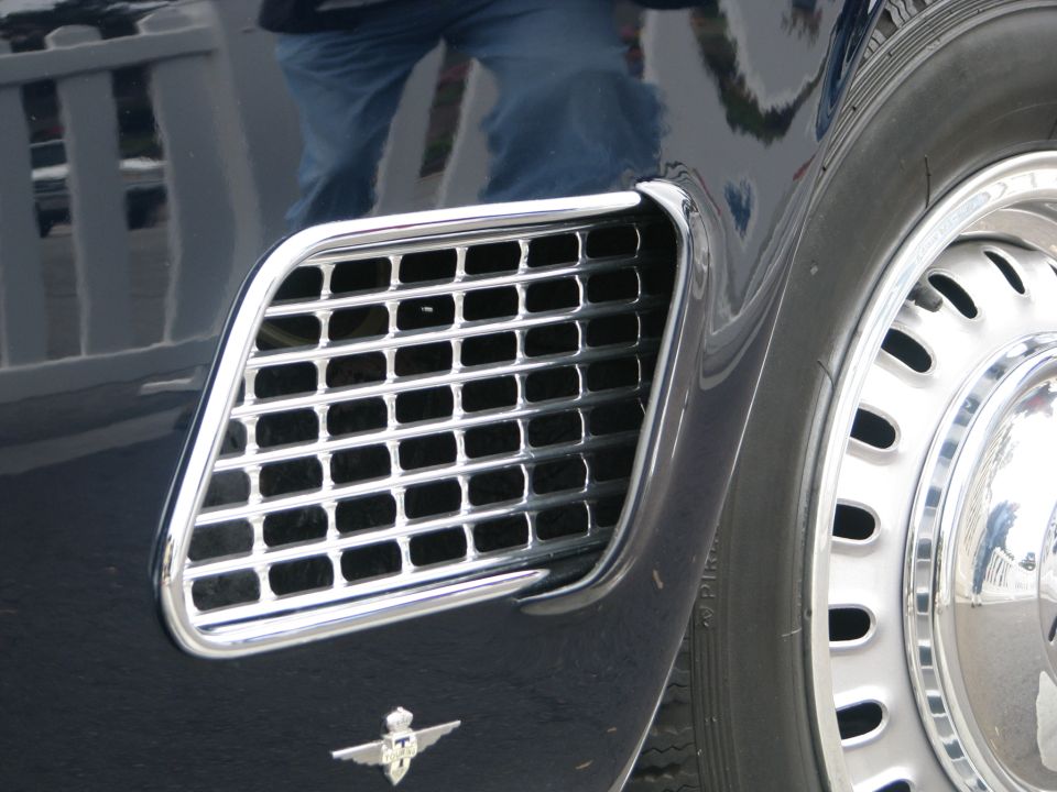 Close-up of a chrome grille vent and a wire-spoke wheel on a dark car