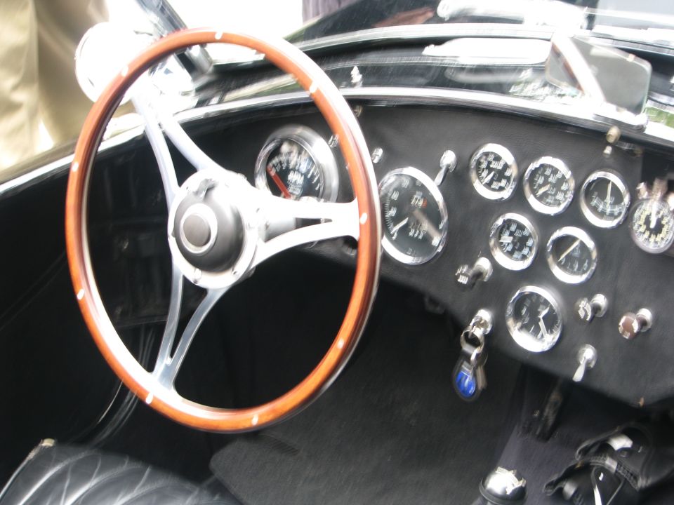 Wood-rimmed steering wheel and black dash with many chrome gauges in a classic roadster