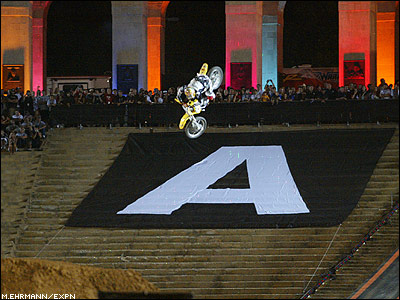 1990 Ford Bronco - A motocross rider performs a stunt in the air above a large 'A' graphic during an event.