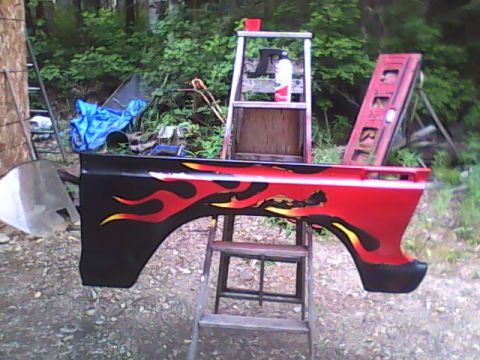 1978 Ford Bronco - A red and black fender with flame decals is displayed outdoors, supported by a wooden step ladder.