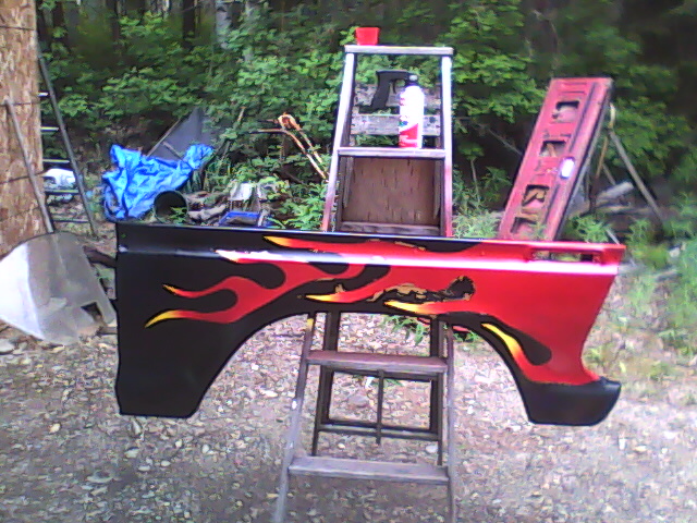 Black fender with red and yellow flames drying on a sawhorse outdoors