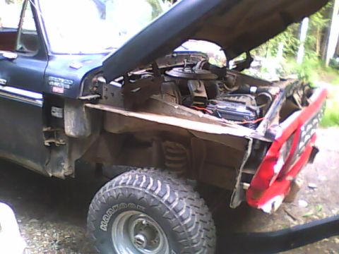 1978 Ford Bronco - The engine bay of a dark SUV is visible with the hood open, showing the engine components and battery.